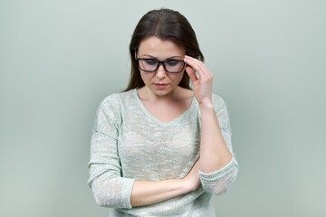 Portrait of alone sad mature woman with glasses on green background