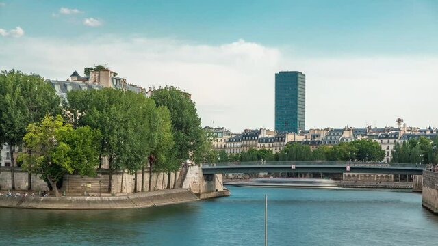 Waterfront of the river Seine near Notre Dame with Saint-Louis bridge timelapse before sunset. View of the houses and trees of the island of Saint-Louis.