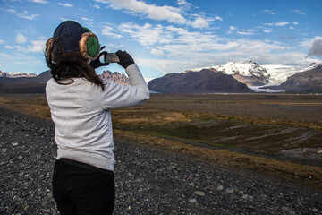 Fototapeta premium SKAFTAFELL NATIONAL PARK, ICELAND - SEPTEMBER 19, 2018: Tourist takes a picture of Skaftafell glaciers from the road. Snow and mountains in the background of a vast field.