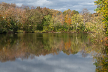 Fototapeta na wymiar Reflection of fall trees on a lake. Beautiful cloudy fall day at the lake with colors of fall leaves reflecting on the river.