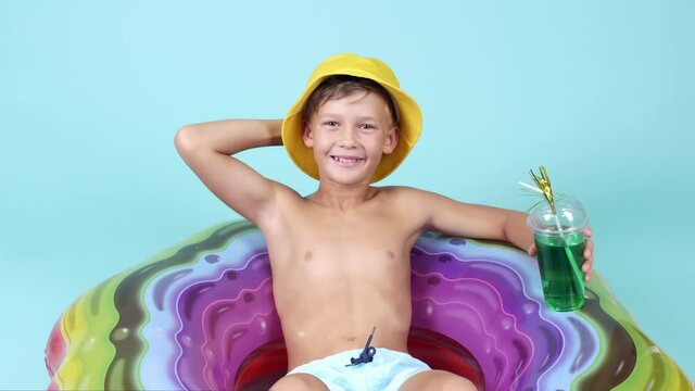 Cute little boy with cocktail relaxing on inflatable ring against color background