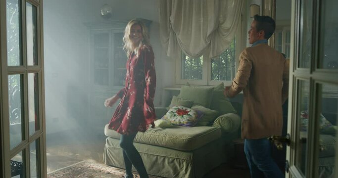 Cinematic shot of young carefree happy smiling homosexual female gay and transgender man couple in love is enjoying time together and having fun to dance together while listening to the music at home.