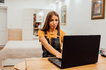 Beautiful young businesswoman working on a laptop while talking to a mobile phone.