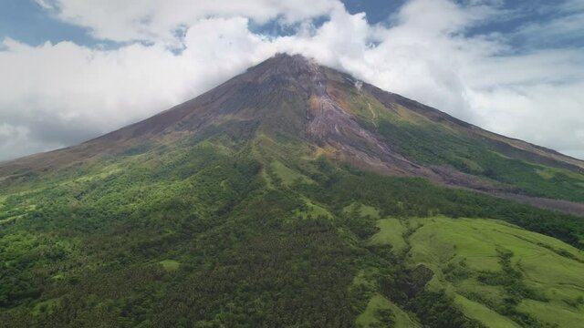 Closeup volcano top erupt clouds of haze aerial. Green grass mountain with hiking path. Philippines landmark of Mayon Mount, Legazpi countryside. Nobody nature landscape at fog. Cinematic drone shot