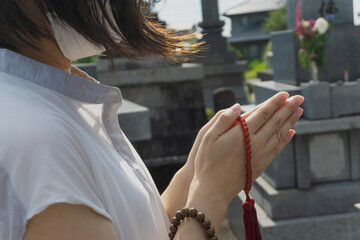 The woman who wore a mask for the infection prevention prays. we photographed it in a Japanese graveyard. 感染予防のマスクをした女性が祈る、お参りする。日本の墓地で撮影しました