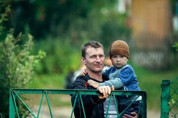 Happy man holds his young son in his arms, on street in the village.