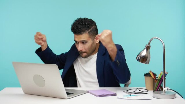 Extremely angry aggressive businessman trying to turn on laptop going to punch faulty computer, problems at work. Indoor studio shot isolated on blue background
