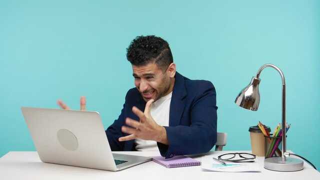 Angry nervous man screaming working at laptop in office, disappointed with broken computer and data lost, deadline. Indoor studio shot isolated on blue background