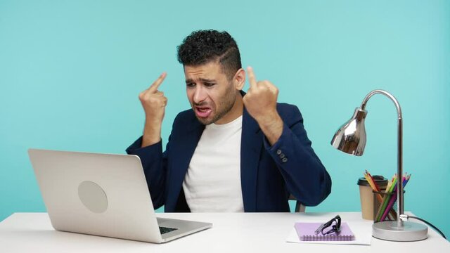 Rude impolite business man showing middle finger to web camera, chatting with companions, negative aggressive man showing fuck sign. Indoor studio shot isolated on blue background