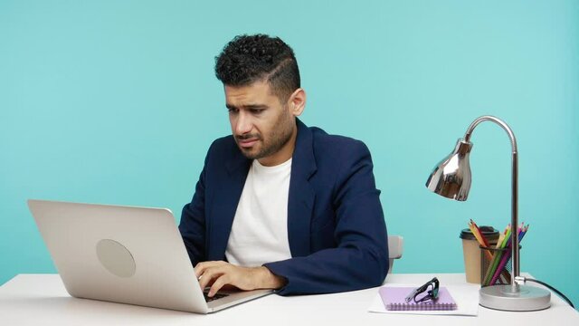 Self confident rude man showing middle finger fuck gesture at camera asking to get off, working on laptop. Indoor studio shot isolated on blue background