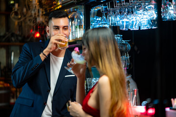 Handsome caucasian man standing at bar counter flirting and talking to beautiful woman with enjoy alcoholic drink cocktail at nightclub party. Smiling couple enjoy romantic dating together at the bar.