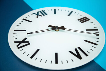White clock with black Roman numerals and blue and light blue background, photo taken with dynamic perspective and selective focus.