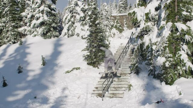 Snowboarder doing a trick on a hand rail in the snow covered forest terrain