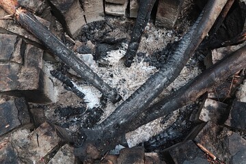 Detail of old circular firepit made of heat resistant bricks, with some large burnt canes and pieces of wood inside. 