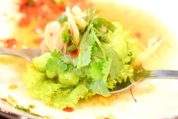 Fresh Shrimp in fish sauce mixed with herbs, garlic, chili  on spoon ready to eat with background of spicy red chili sauce on plate 