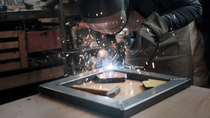 Worker wearing a mask and gloves soldering metal parts