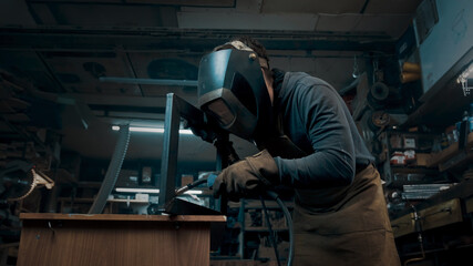 Worker wearing a mask and gloves soldering metal parts