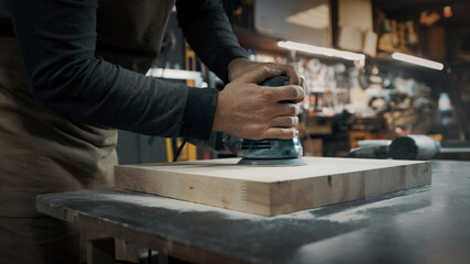 A carpenter grinds a piece of wood for a loft-style chair. Close up.