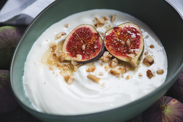 Close-up of greek yogurt served with fig fruits, honey and chopped walnuts in a green bowl, horizontal shot, selective focus
