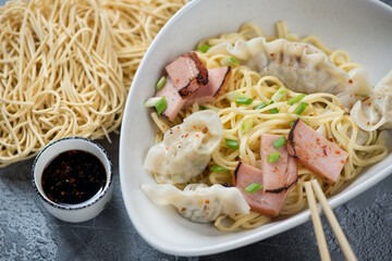 Grey bowl with Kon Lo Wantan Mee or egg noodles with wontons and char siu, close-up, studio shot