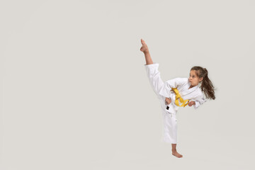 Full length shot of little karate girl in white kimono with a yellow sash exercising and fighting, doing martial arts, standing isolated over white background © Svitlana
