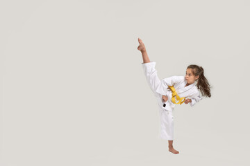 Full length shot of little karate girl in white kimono with a yellow sash exercising and fighting,...