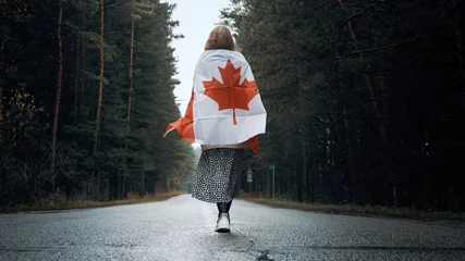 Papier Peint photo autocollant Canada A girl in a white sweater and skirt walks through the forest holding the flag of canada
