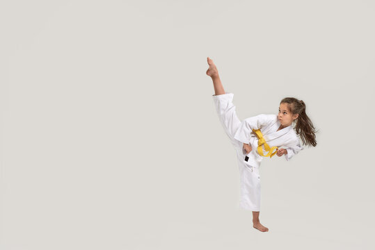 Full length shot of little karate girl in white kimono with a yellow sash exercising and fighting, doing martial arts, standing isolated over white background