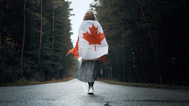 A Girl In A White Sweater And Skirt Walks Through The Forest Holding The Flag Of Canada