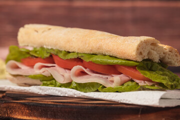 Ham, tomato and lettuce sandwich on a plate on a rustic background