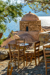 Traditional cafe exterior in the fortified medieval  castle of Monemvasia. Iron tables and wooden chairs with the view of St. Nicholas Church and the  aegean sea in the background.