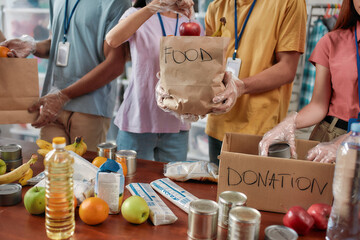 Cropped shot of male and female volunteers holding paper bag with food while packing donation for needy people, Young team working in charitable foundation