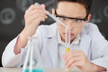 Concentrated young Vietnamese boy adding reagent in test tube with yellow liquid