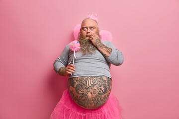 Plump bearded man stares bugged eyes dressed in fairy or princess costume entertains children on...