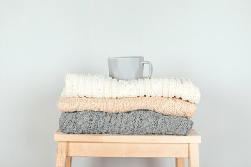 A stack of knitted sweaters and coffee mug. The concept of winter comfort and cozy.