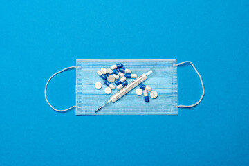 Fototapeta na wymiar Protective medical face mask,Thermometer and pills on a blue background - Top view with copy space