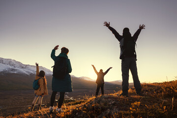 Four young hikers greetings sunset in mountains