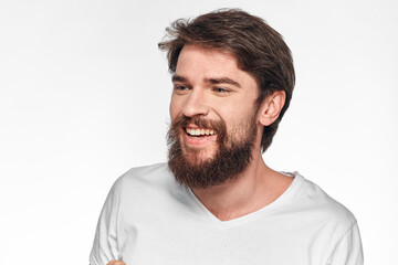 cheerful bearded man in a white t-shirt emotions gestures with his hands light background studio