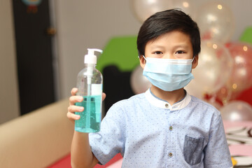 Asian boy with protection face mask holding alcohol antiseptic gel at party event, prevent against infection of Covid-19 outbreak,  new normal lifestyle