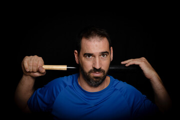 Bearded man dressed in blue t-shirt in defiant pose posing whit a baseball bat on black background