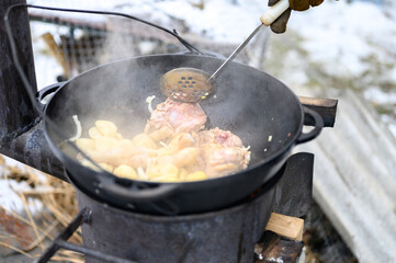 cooking in winter in a cauldron in the open air on a fire on a cast iron stove. food from potatoes, onions and chicken meat is prepared in a cast iron cauldron