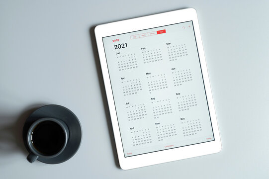 a tablet with an open calendar for 2021 year and a cup of coffee on a gray background