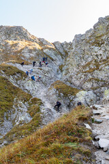 Many tourists climbing steep trail with chains towards Szpiglasowa Pass in Tatra Mountains, Poland, autumn.