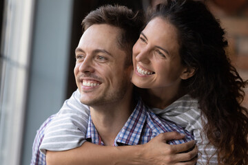 Obraz premium Close up of excited young Caucasian couple hug look in distance dreaming or thinking happy bright future together. Smiling man and woman imagine visualize new perspectives. Vision, marriage concept.