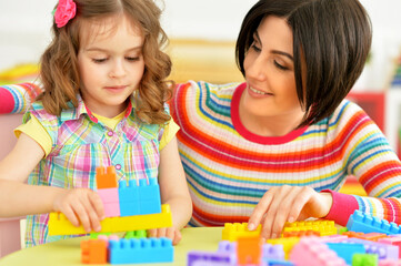Fototapeta premium Cute little girl and her mother playing colorful plastic blocks together