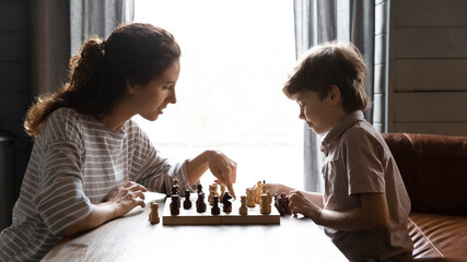 Wide banner panoramic view of young Caucasian mother engaged in board game with little son. Loving mom have fun play chess game with small smart 7s boy child, involved in creative logical thinking.