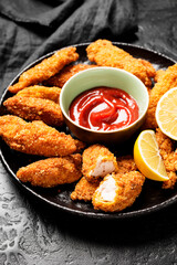 Delicious crispy fried breaded chicken breast strips on black background.