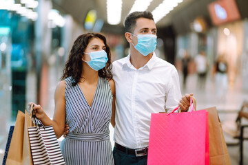 Beautiful young loving couple  in protective sterile medical mask carrying shopping bags and enjoying together. Shopping in the coronavirus epidemic. Purchases, black friday, discounts, sale concept.