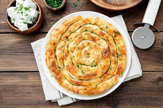 Traditional feta cheese phyllo pastry pie on wooden background .	