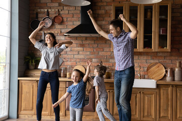 Overjoyed young Caucasian family with two small kids dance in new own renovated kitchen together. Happy parents with little children renters tenants have fun at home, engaged in funny activity.